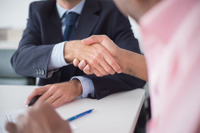 Person wearing a suit shaking hands with a person in a pink shirt